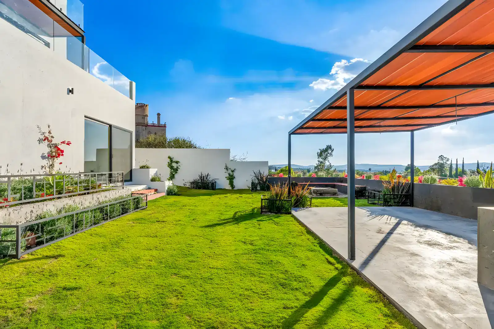 Casa de la Vista, garden lawn with a steel pergola with a wood-toned roof, raised planters and a view of the valley, San Miguel de Allende