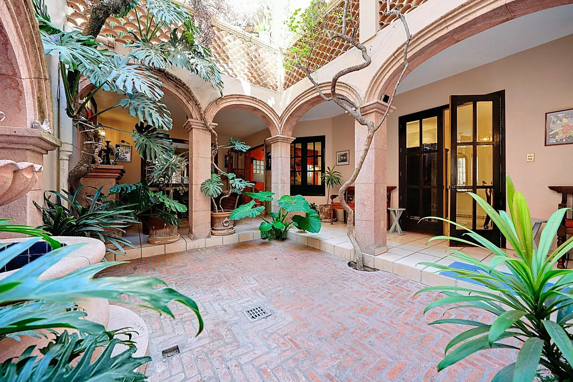 Casa de las Cruces, arched courtyard with a brick floor, tropical plants and glass-paneled doors under a trellis, San Miguel de Allende