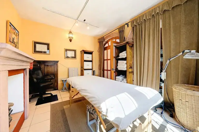 Casa de las Cruces, treatment room with a massage table, a stone fireplace and draped windows, San Miguel de Allende