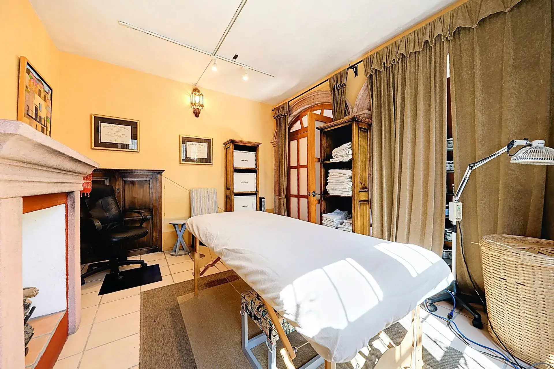 Casa de las Cruces, treatment room with a massage table, a stone fireplace and draped windows, San Miguel de Allende