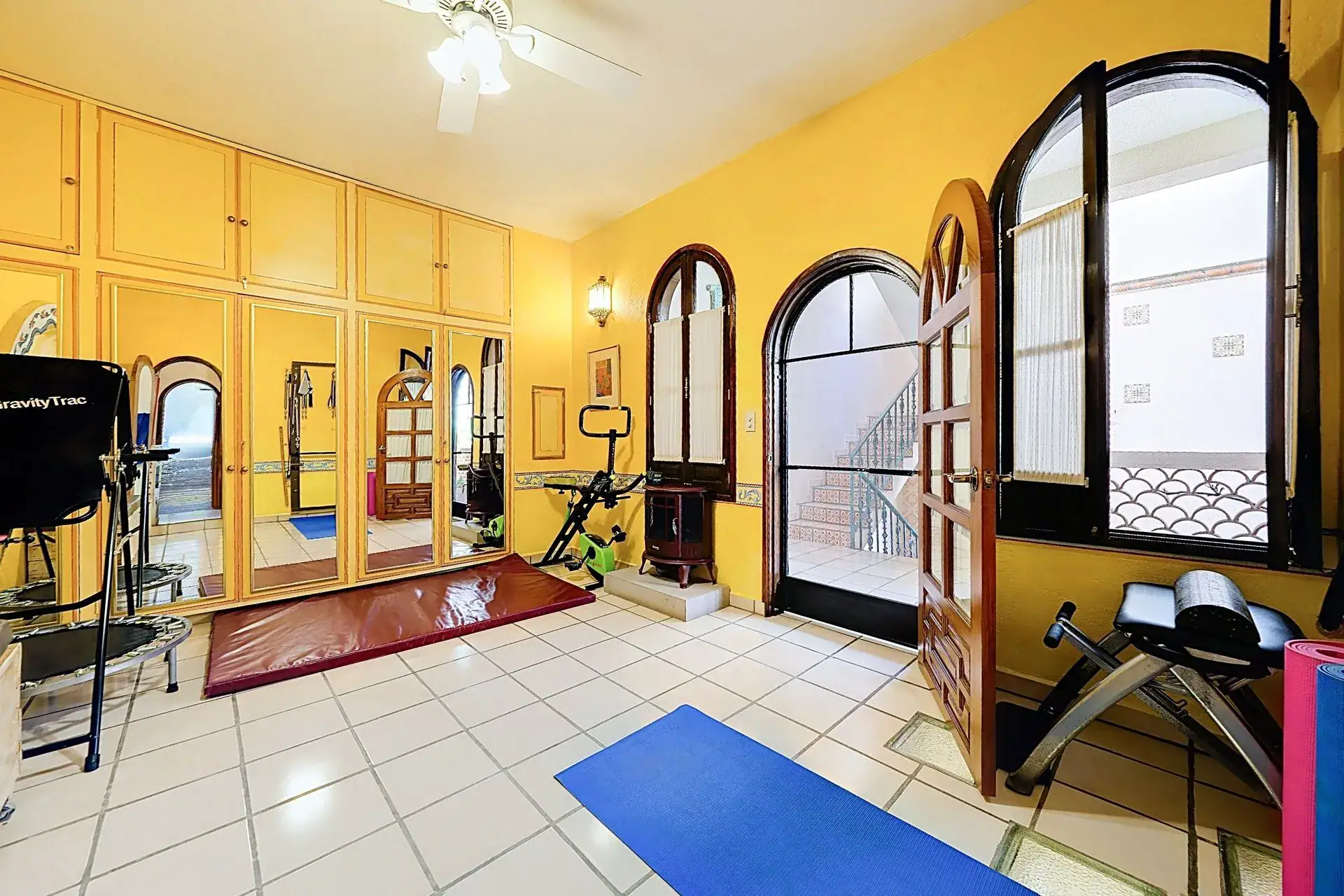 Casa de las Cruces, yellow exercise room with built-in cabinets, arched windows and fitness equipment, San Miguel de Allende