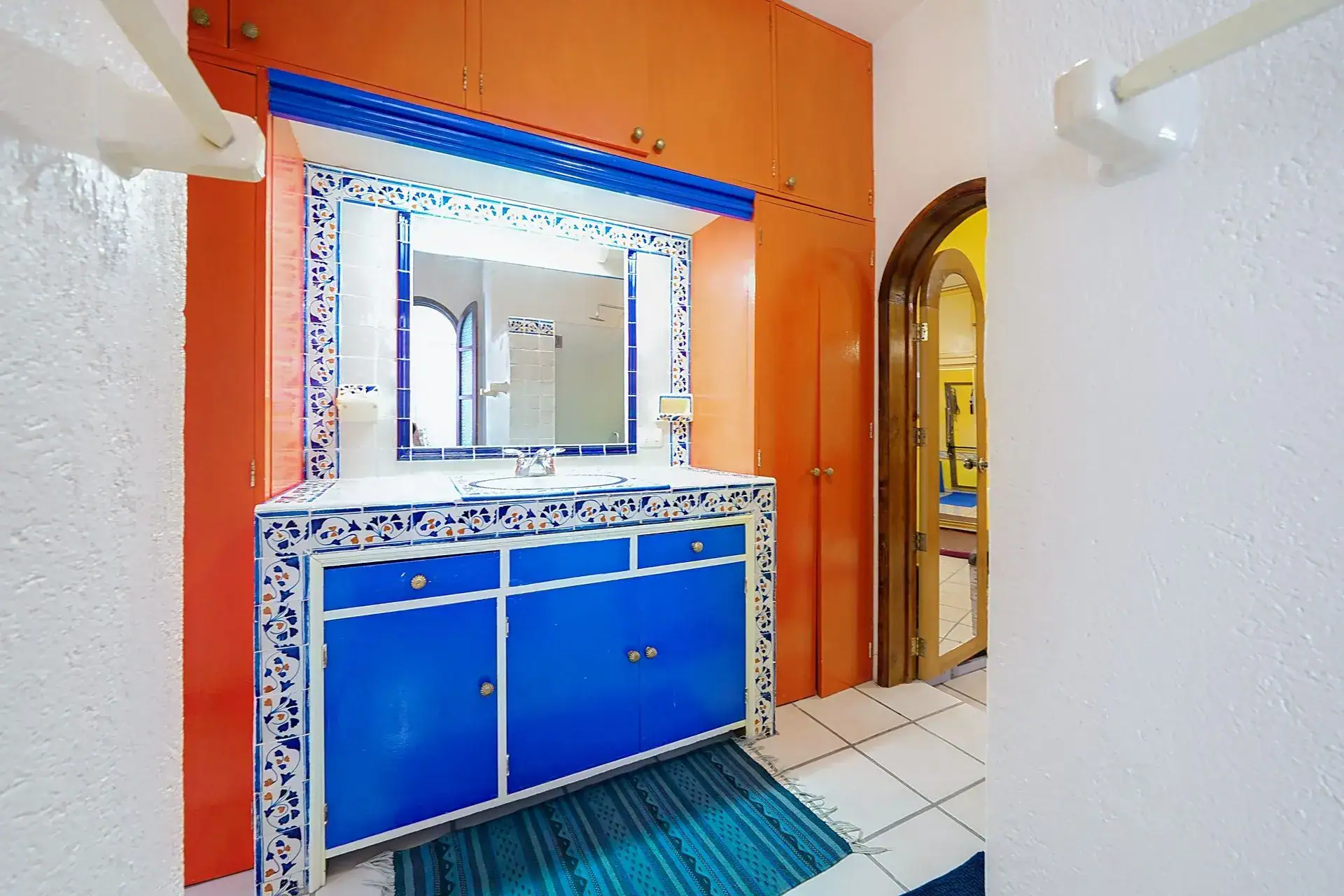 Casa de las Cruces, bathroom vanity with a blue cabinet, tiled mirror frame and an orange wall, San Miguel de Allende