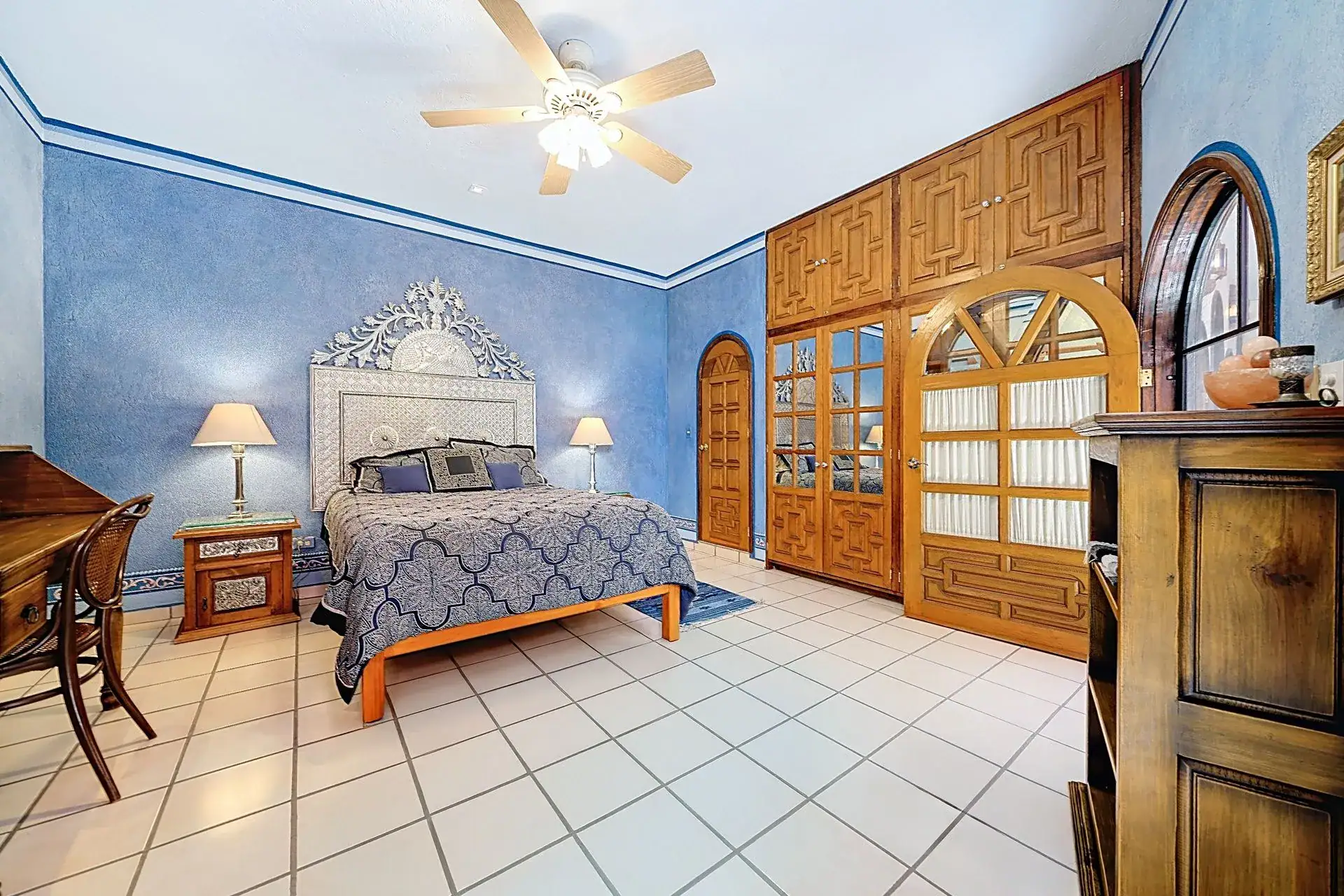 Casa de las Cruces, bedroom with a blue wall, a carved metal headboard and carved wood double doors, San Miguel de Allende