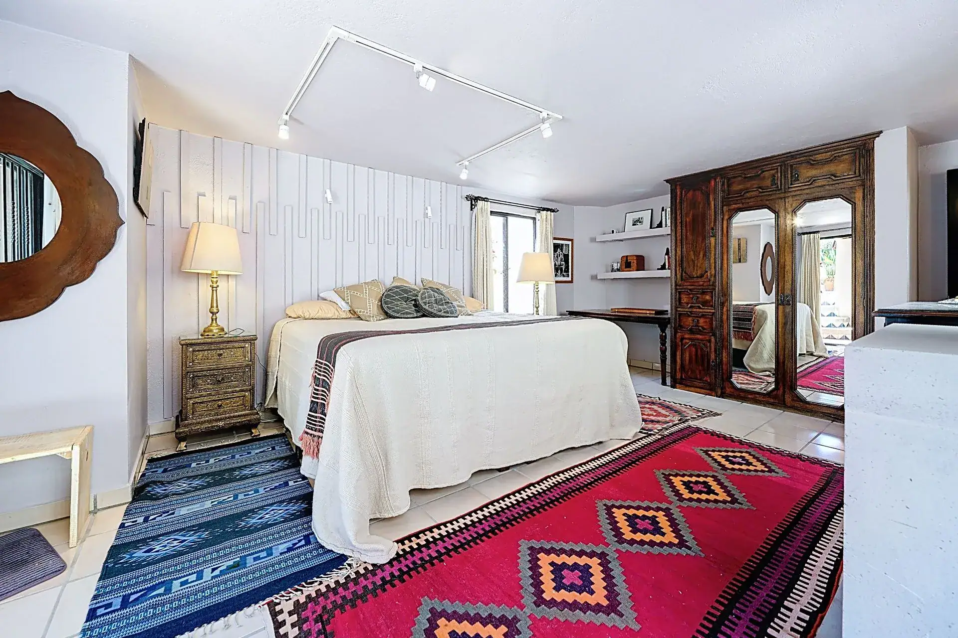 Casa de las Cruces, bedroom with a white-paneled wall, a bed with a striped throw and red geometric rugs, San Miguel de Allende
