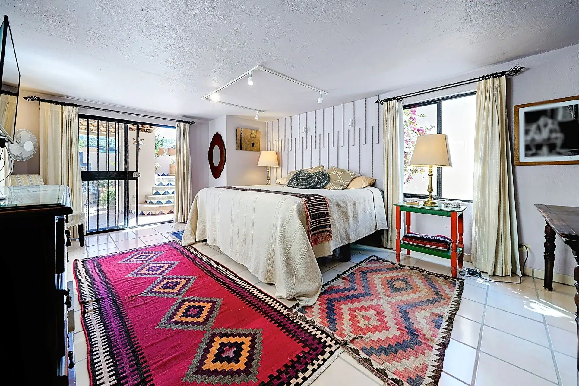 Casa de las Cruces, bedroom with a red and orange rug, a desk and a window to the patio, San Miguel de Allende