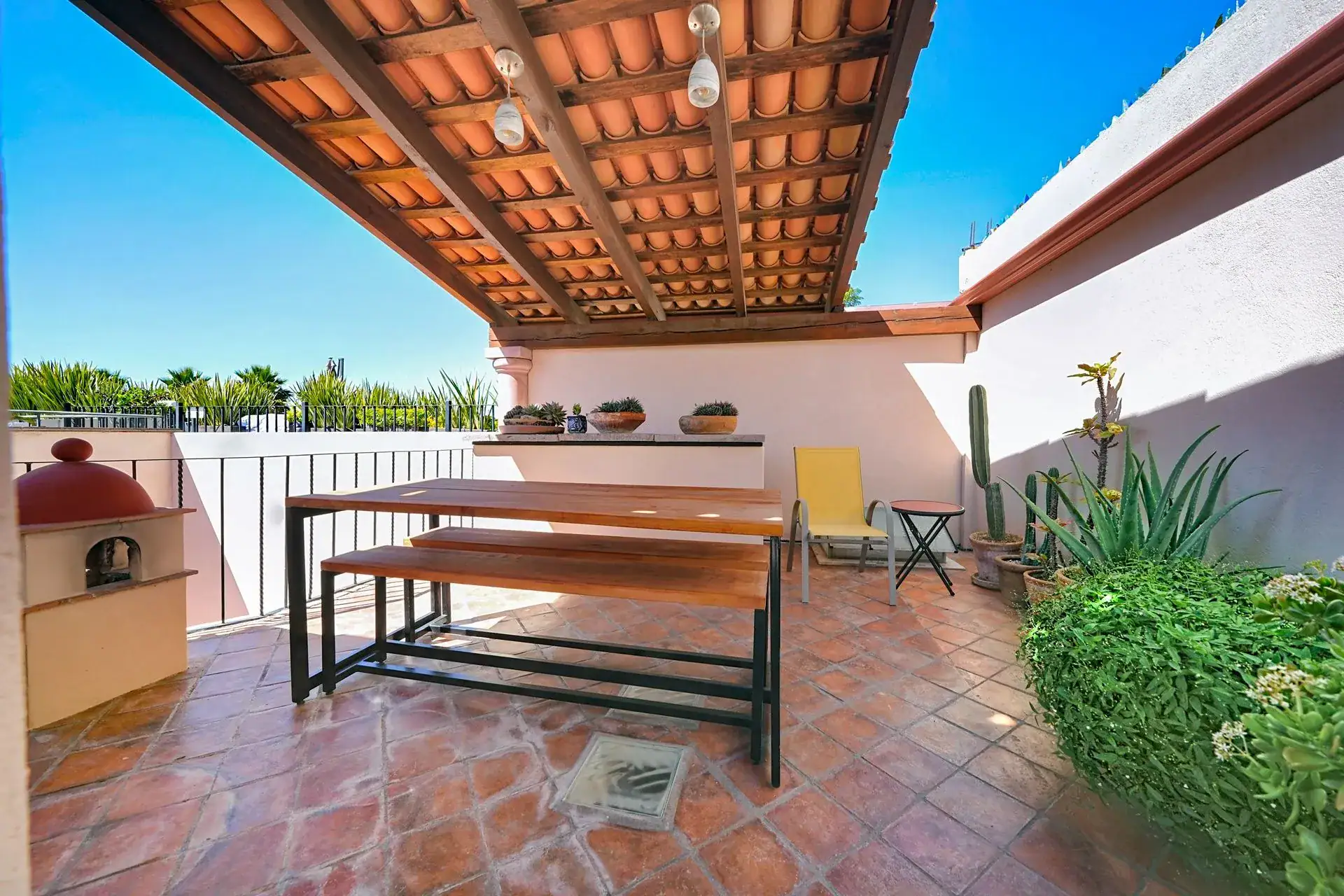 Casa de las Cruces, rooftop terrace with a wooden bench table, a clay oven and potted plants, San Miguel de Allende