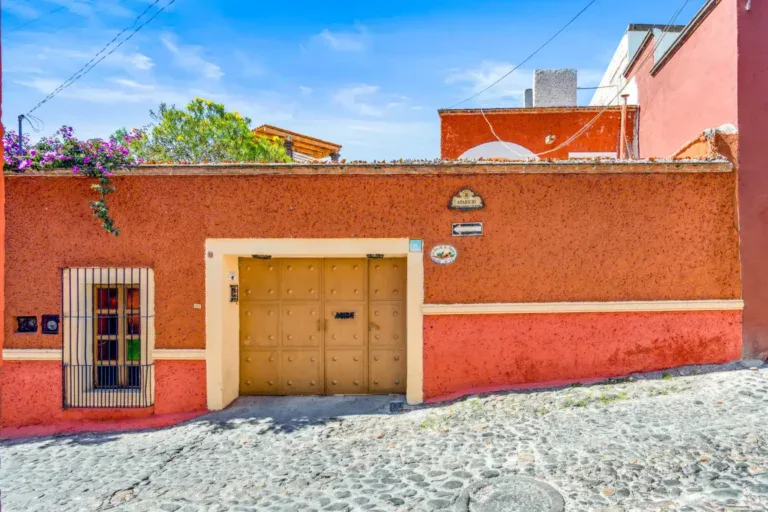 Casa de los Espejos, terracotta street facade with a wood garage door and a barred window, San Miguel de Allende