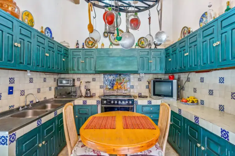 Casa de los Espejos, kitchen with teal cabinets, a pot rack and a round wood table, San Miguel de Allende