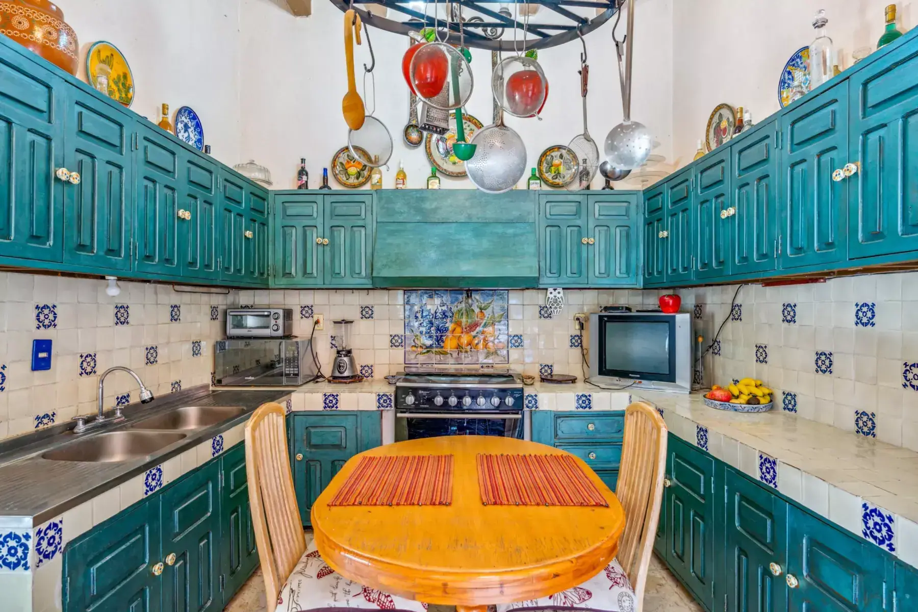 Casa de los Espejos, kitchen with teal cabinets, a pot rack and a round wood table, San Miguel de Allende