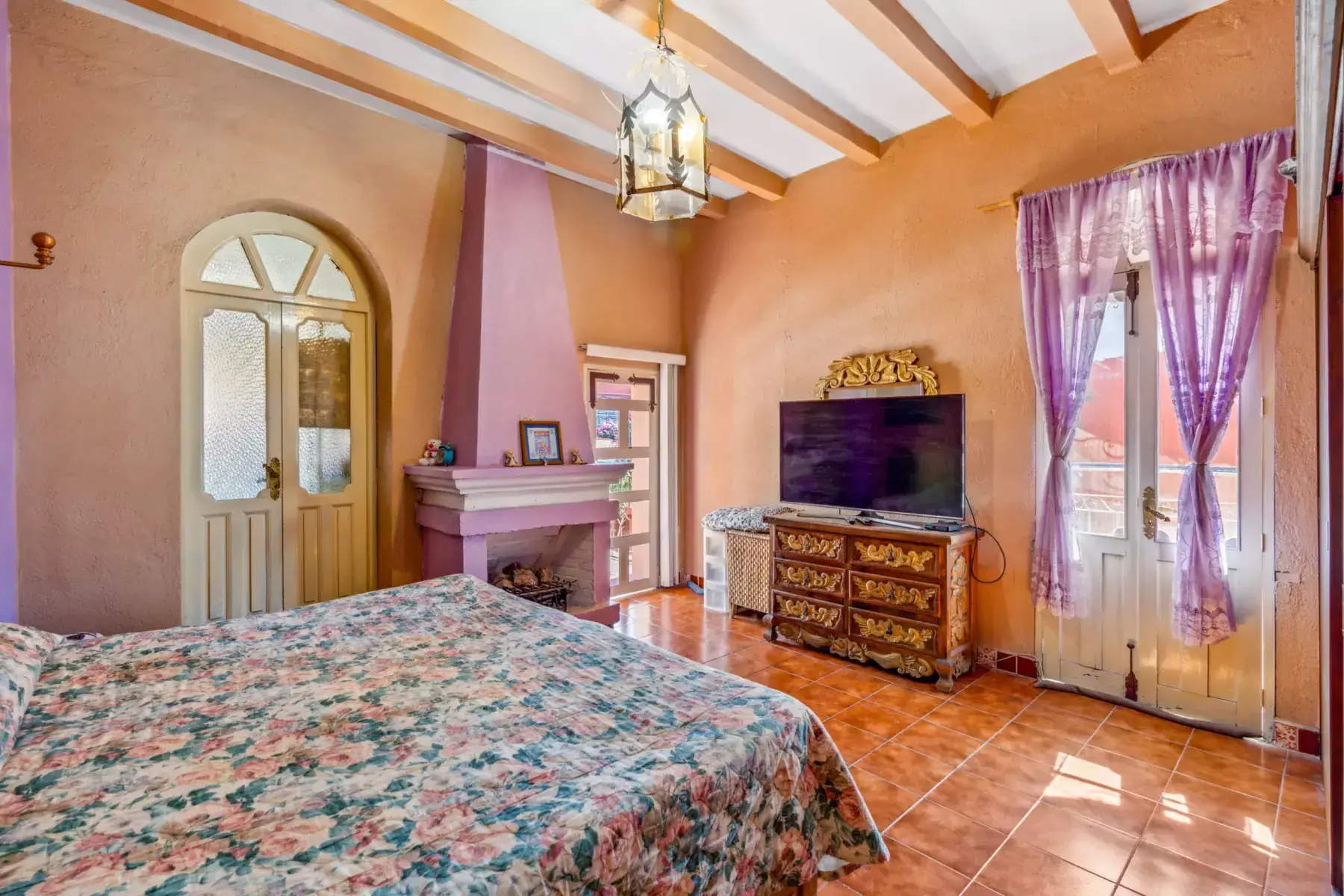 Casa de los Espejos, bedroom with a corner fireplace and a TV on a wood dresser, San Miguel de Allende