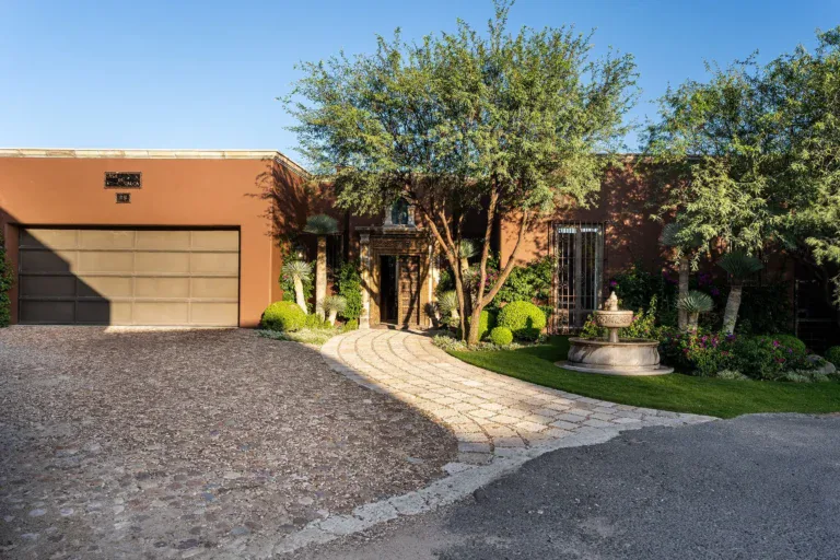Casa de Salca, driveway to a low adobe house with a fountain and a mesquite tree, San Miguel de Allende