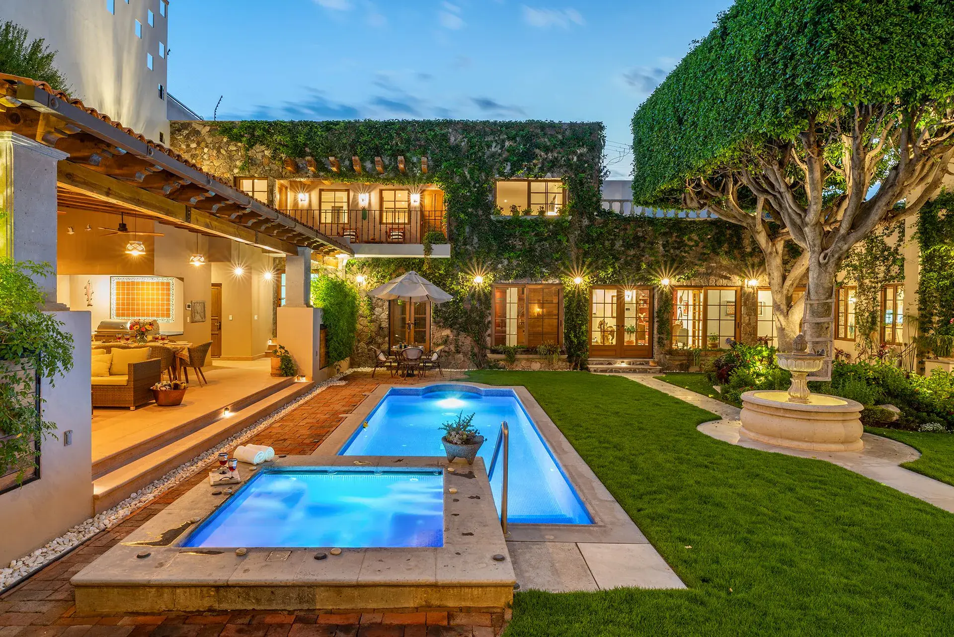 Casa del Angel, courtyard lap pool and spa beside a lawn with glowing windows at dusk, San Miguel de Allende