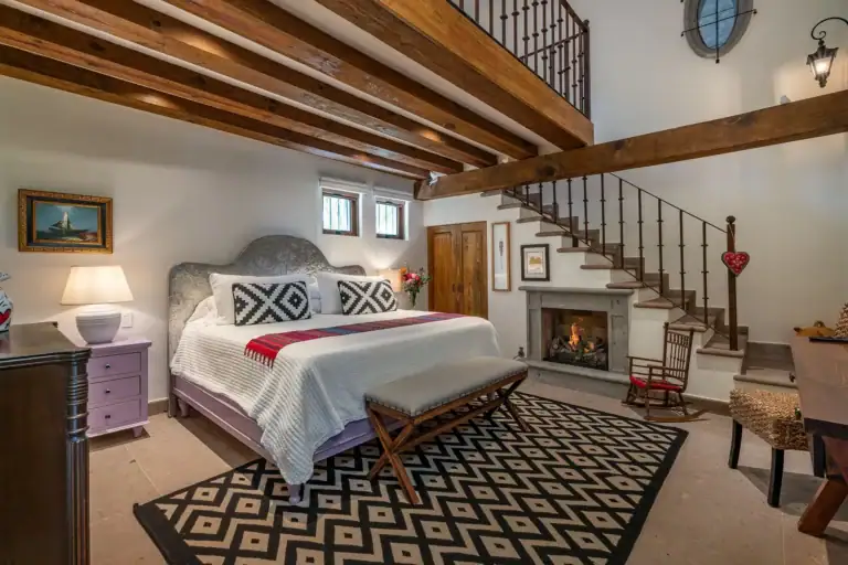 Casa del Angel, primary bedroom with a fireplace, a patterned rug and a staircase, San Miguel de Allende