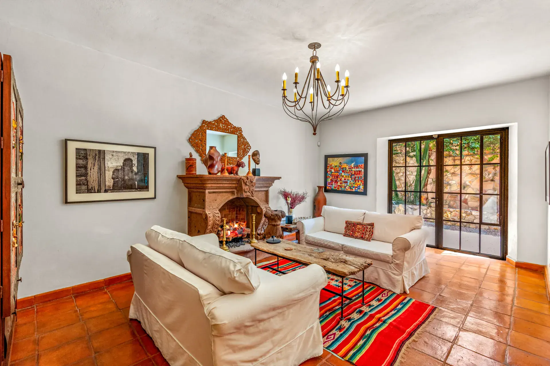 Casa del Artista, living room with white slipcovered sofas, a carved stone fireplace, a striped rug and glass doors to the garden, San Miguel de Allende