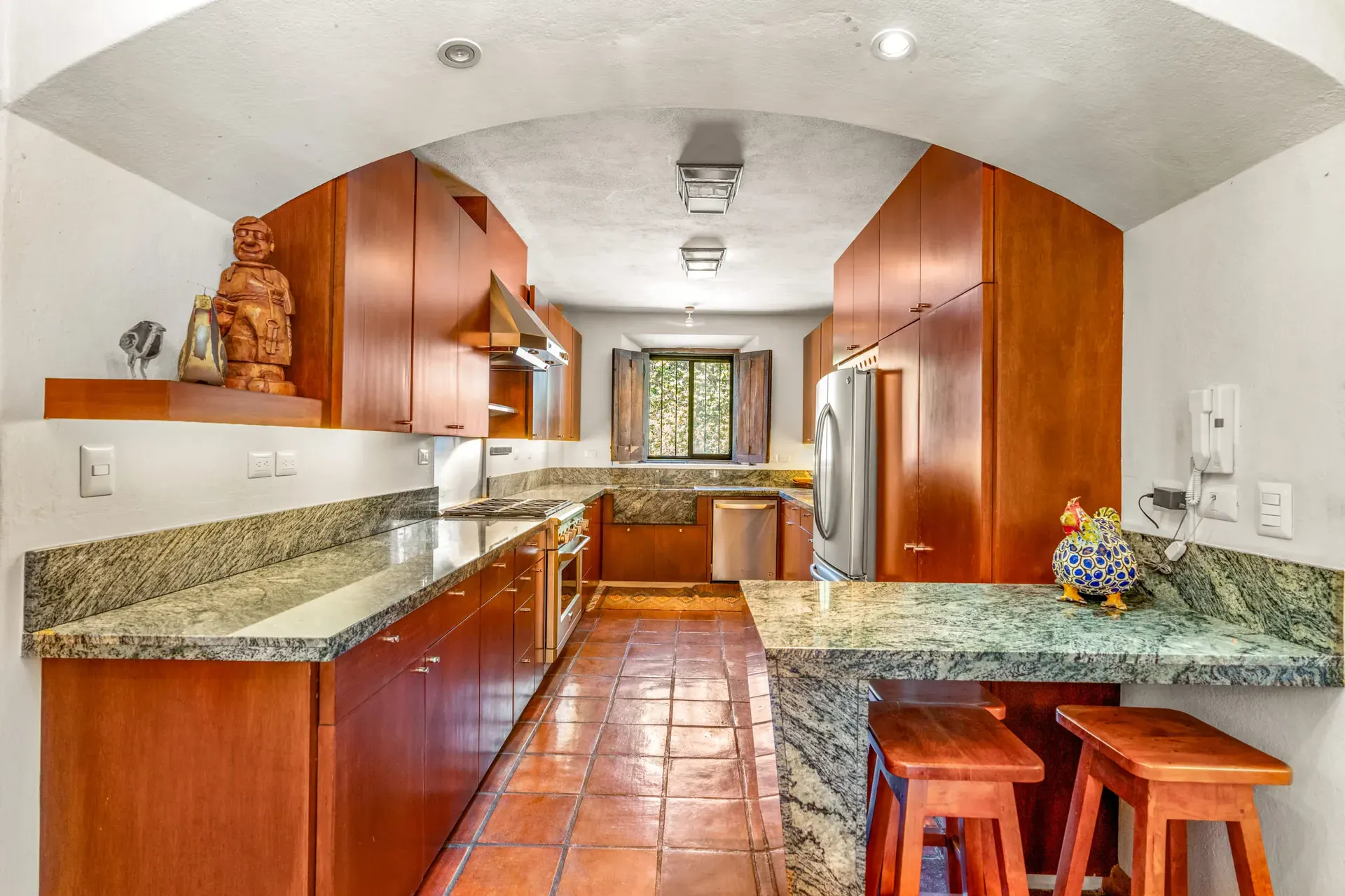 Casa del Artista, galley kitchen with cherry wood cabinets, green granite counters, a stainless range and a breakfast bar with stools, San Miguel de Allende