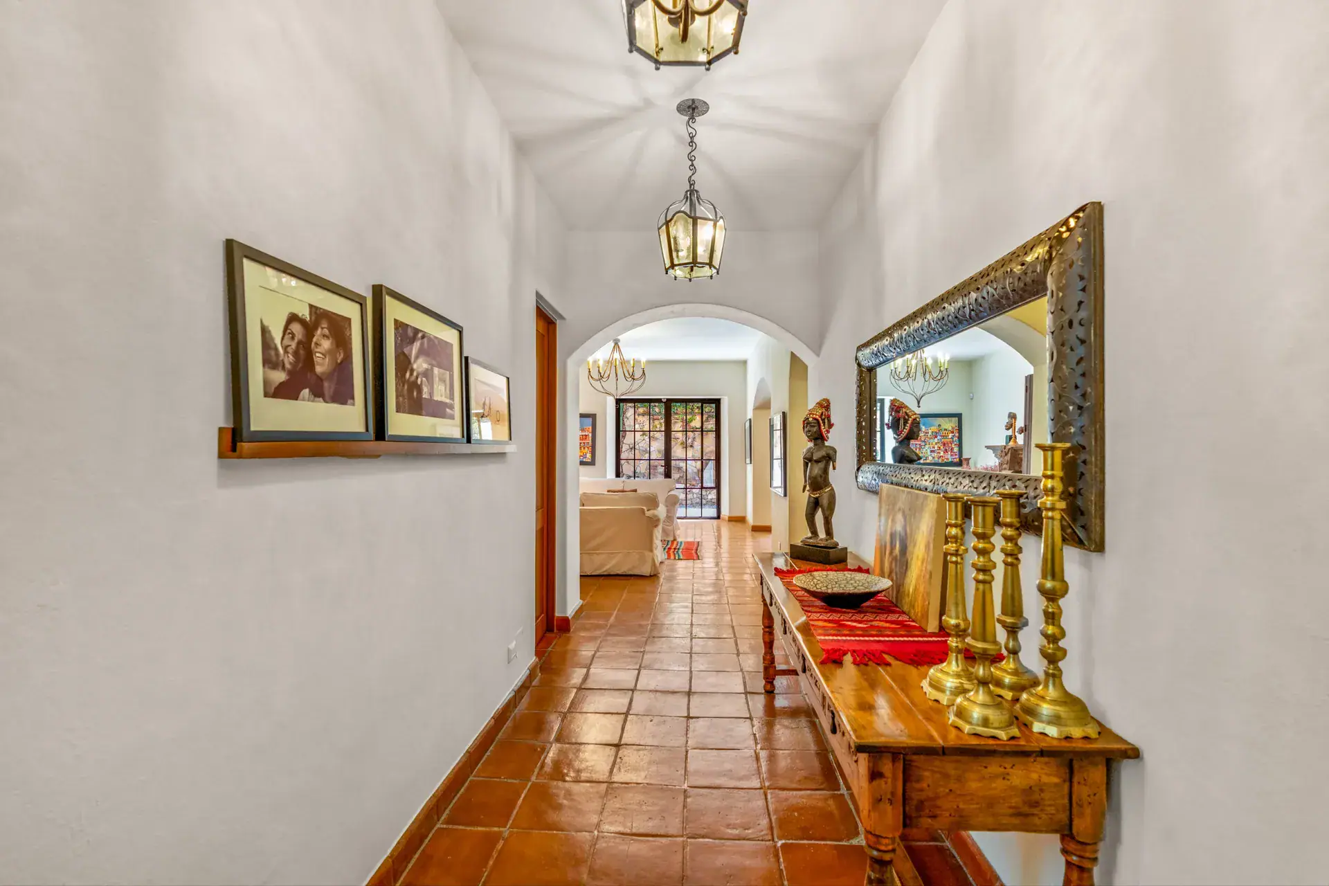 Casa del Artista, long arched hallway with framed photographs, a carved console with brass candlesticks and lanterns, San Miguel de Allende