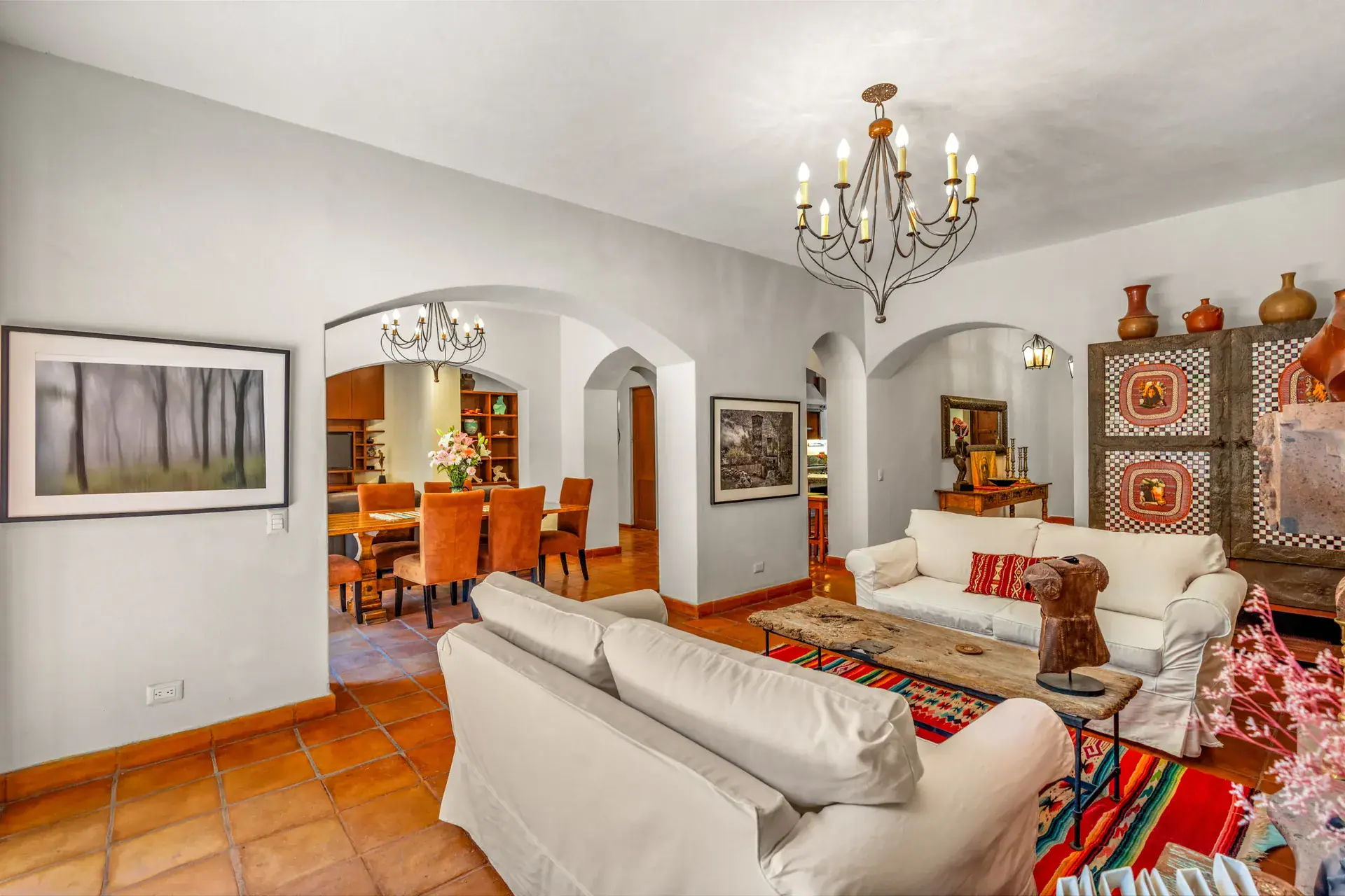 Casa del Artista, living room and dining room beyond an arch, with a painted cabinet and clay pots, San Miguel de Allende