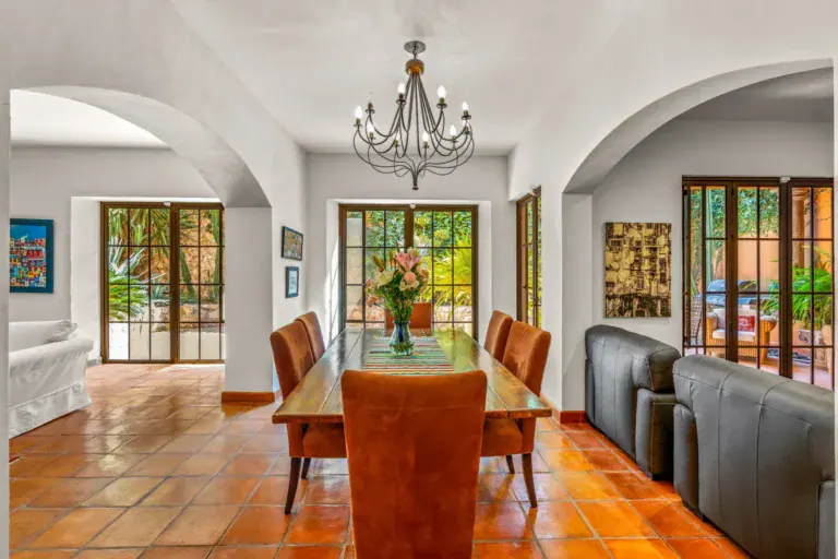 Casa del Artista, dining table and a living room beyond arches with an iron chandelier and glass doors to the patio, San Miguel de Allende