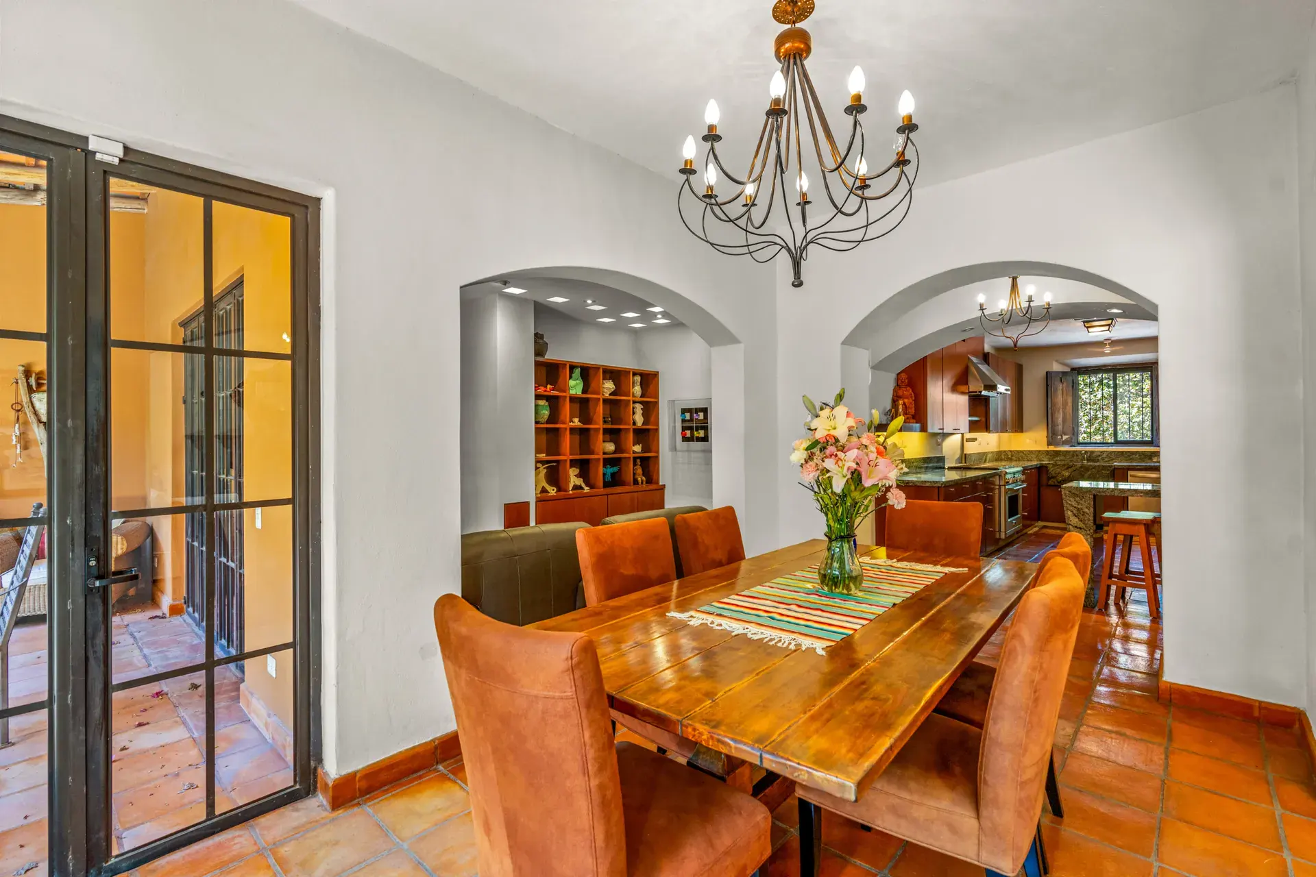 Casa del Artista, dining table with a striped runner beside black-framed glass doors and an arch to the kitchen, San Miguel de Allende