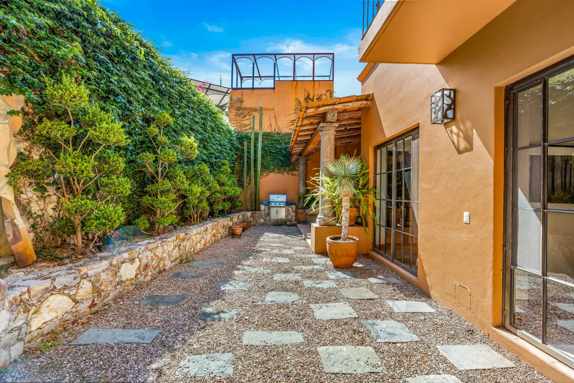 Casa del Artista, gravel courtyard with flagstone pavers, a stone retaining wall and an orange house with glass doors, San Miguel de Allende