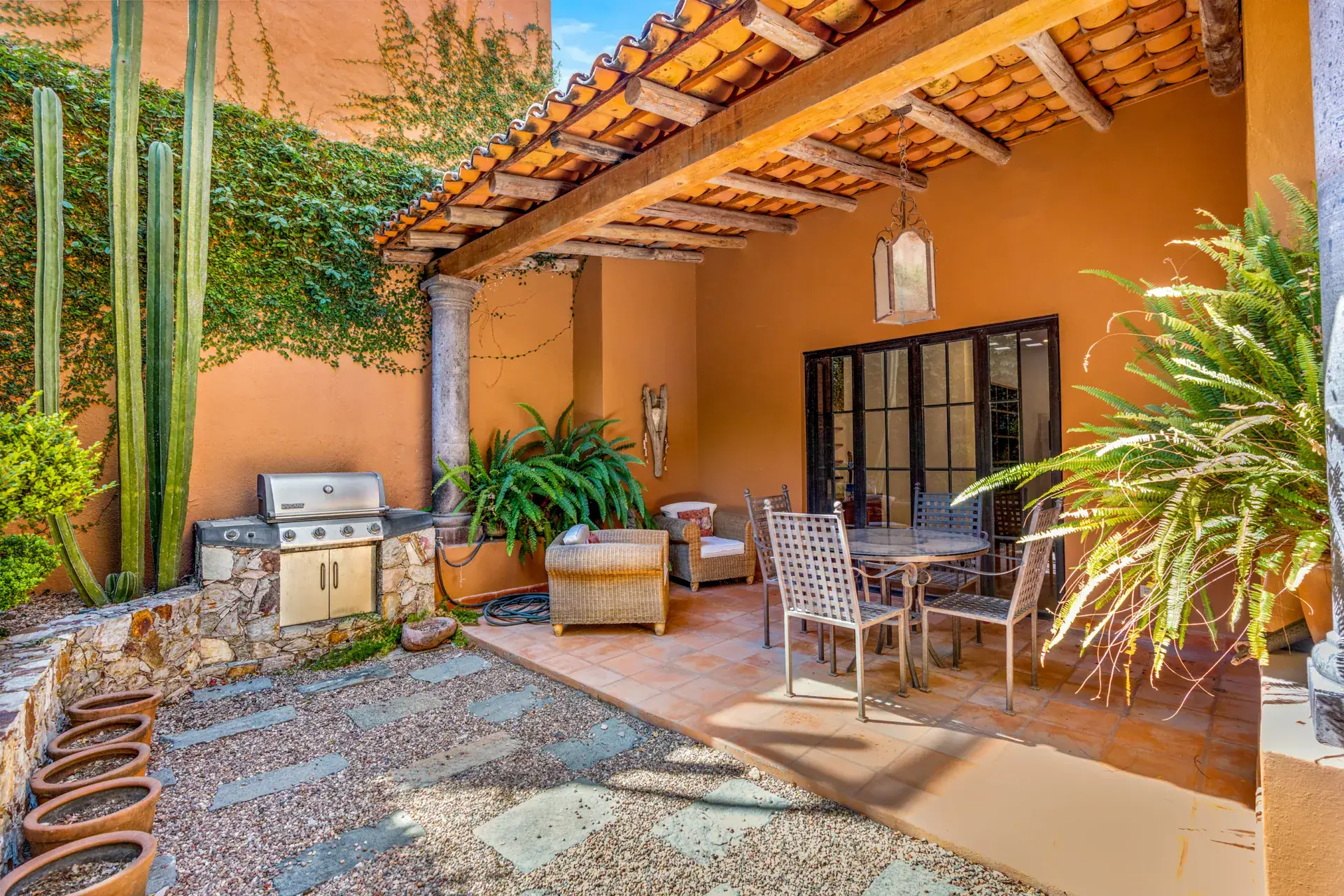 Casa del Artista, covered patio with an outdoor grill, a dining table, tall cactus and a tile roof pergola, San Miguel de Allende
