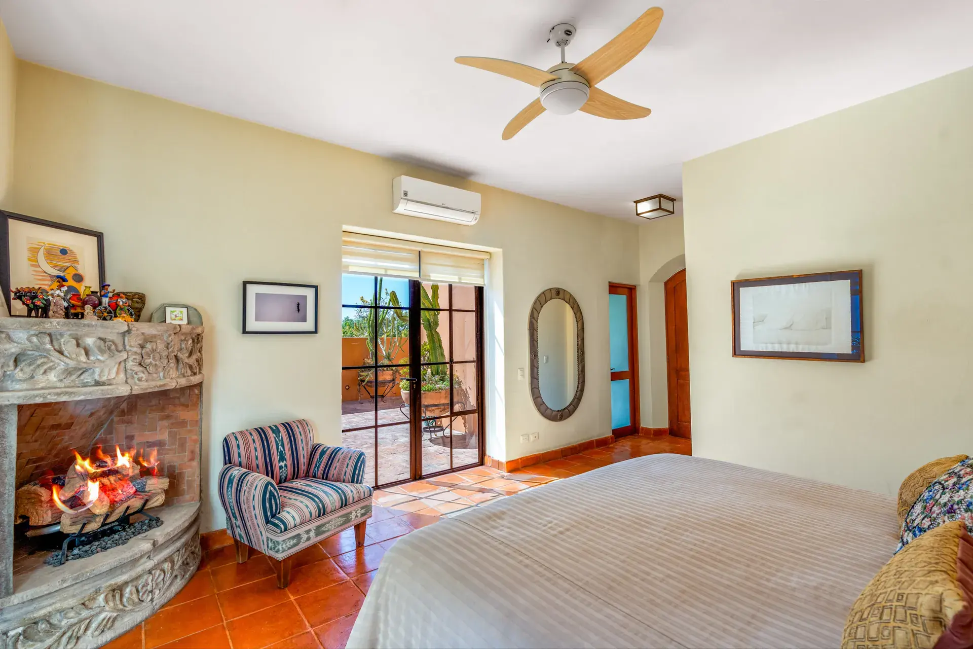 Casa del Artista, bedroom with a ceiling fan, a stone fireplace and glass doors to the patio, San Miguel de Allende