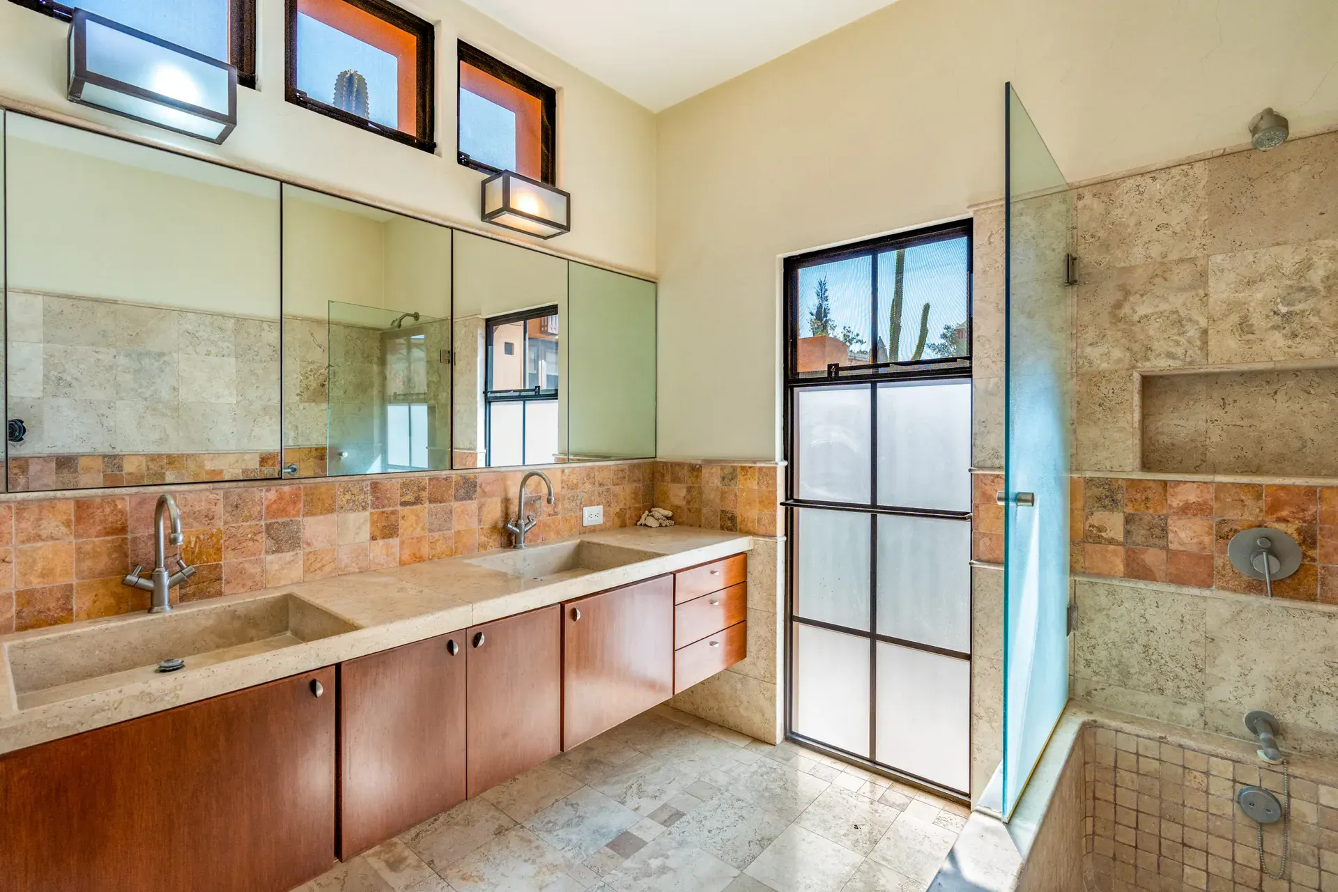 Casa del Artista, bathroom with a long wood vanity, stone trough sinks, a glass shower and a high window, San Miguel de Allende