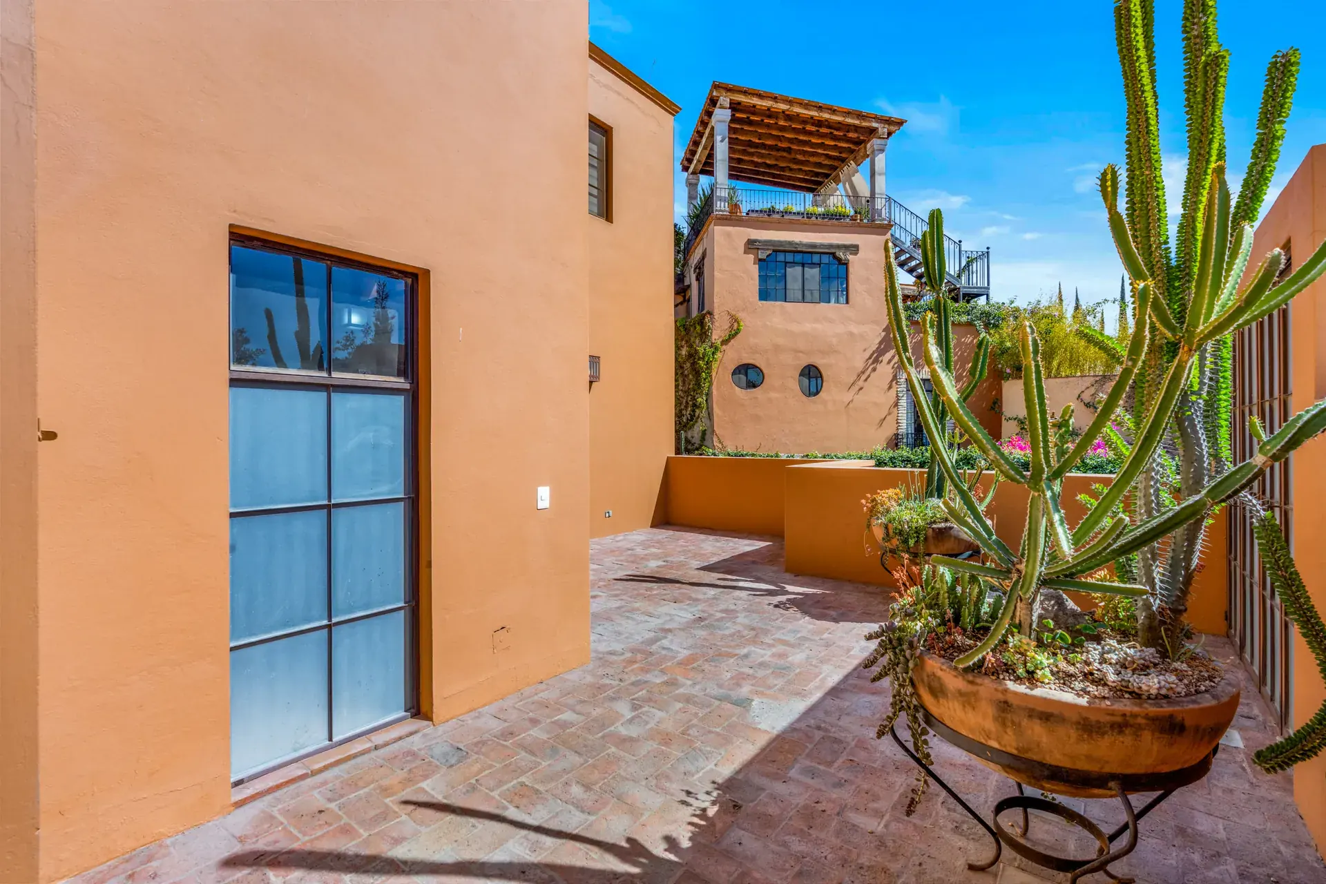 Casa del Artista, side patio wall with a tall glass door, a cactus and a view to the rooftop pavilion, San Miguel de Allende