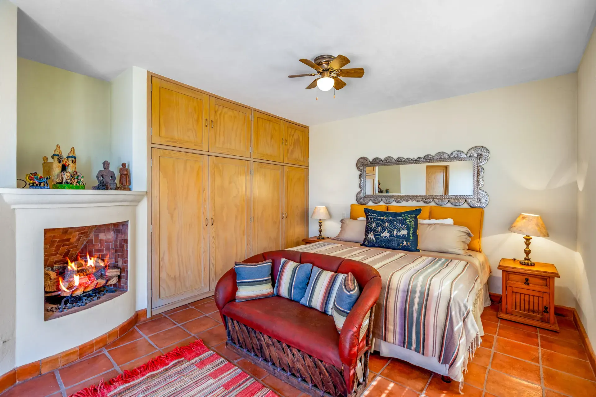 Casa del Artista, bedroom with an iron frame mirror, wood wardrobes, a corner fireplace and a red leather sofa, San Miguel de Allende