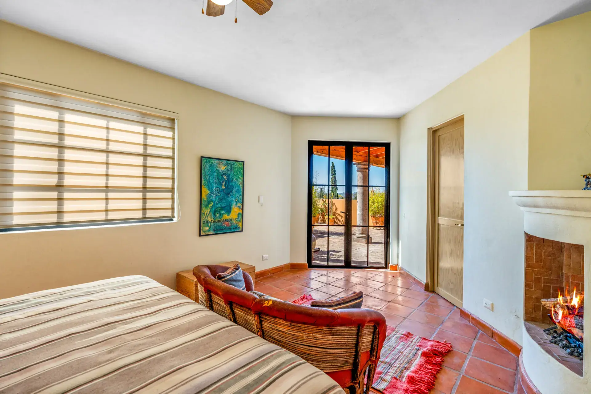 Casa del Artista, bedroom with a striped blanket, a window shade, a green painting and a corner fireplace, San Miguel de Allende