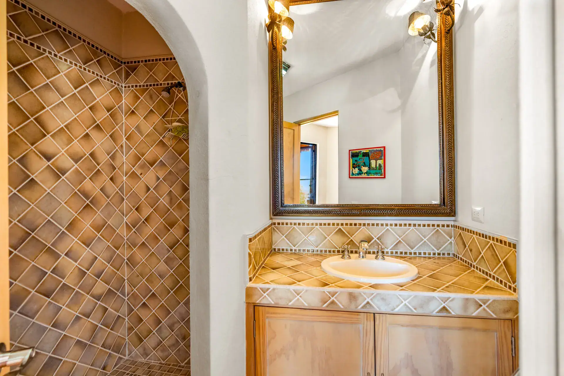 Casa del Artista, bathroom with a diamond-pattern tile wall, a tiled vanity and a gilt mirror, San Miguel de Allende