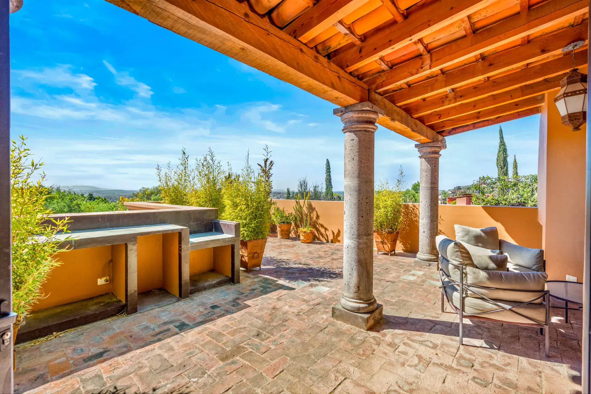 Casa del Artista, covered rooftop terrace with a wood beam roof, stone columns, a built-in counter and a view of the hills, San Miguel de Allende
