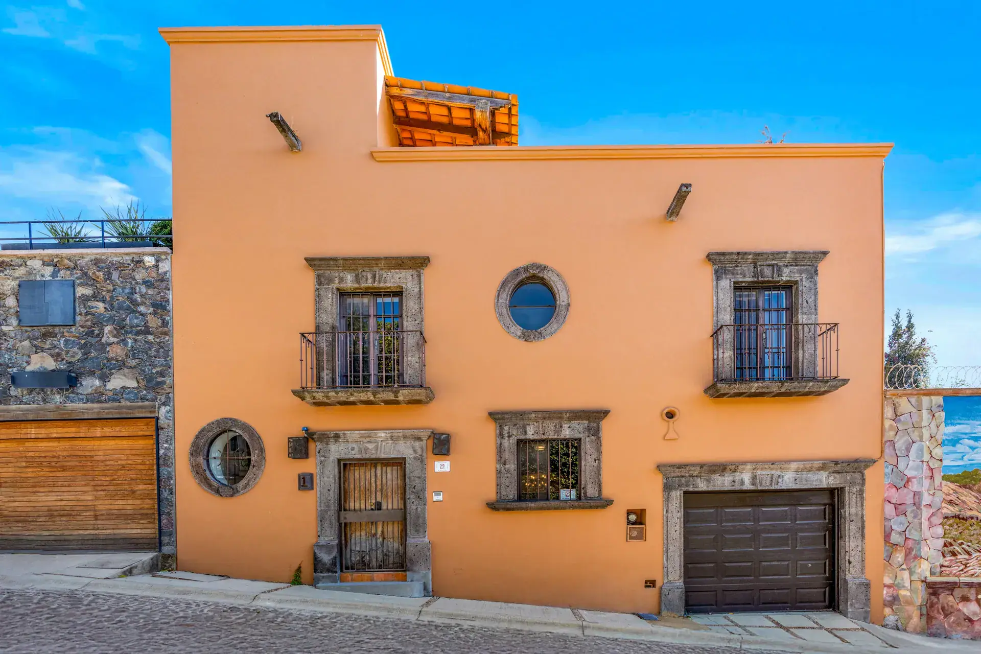 Casa del Artista, orange street facade with two stone-framed windows, round windows and a garage door, San Miguel de Allende