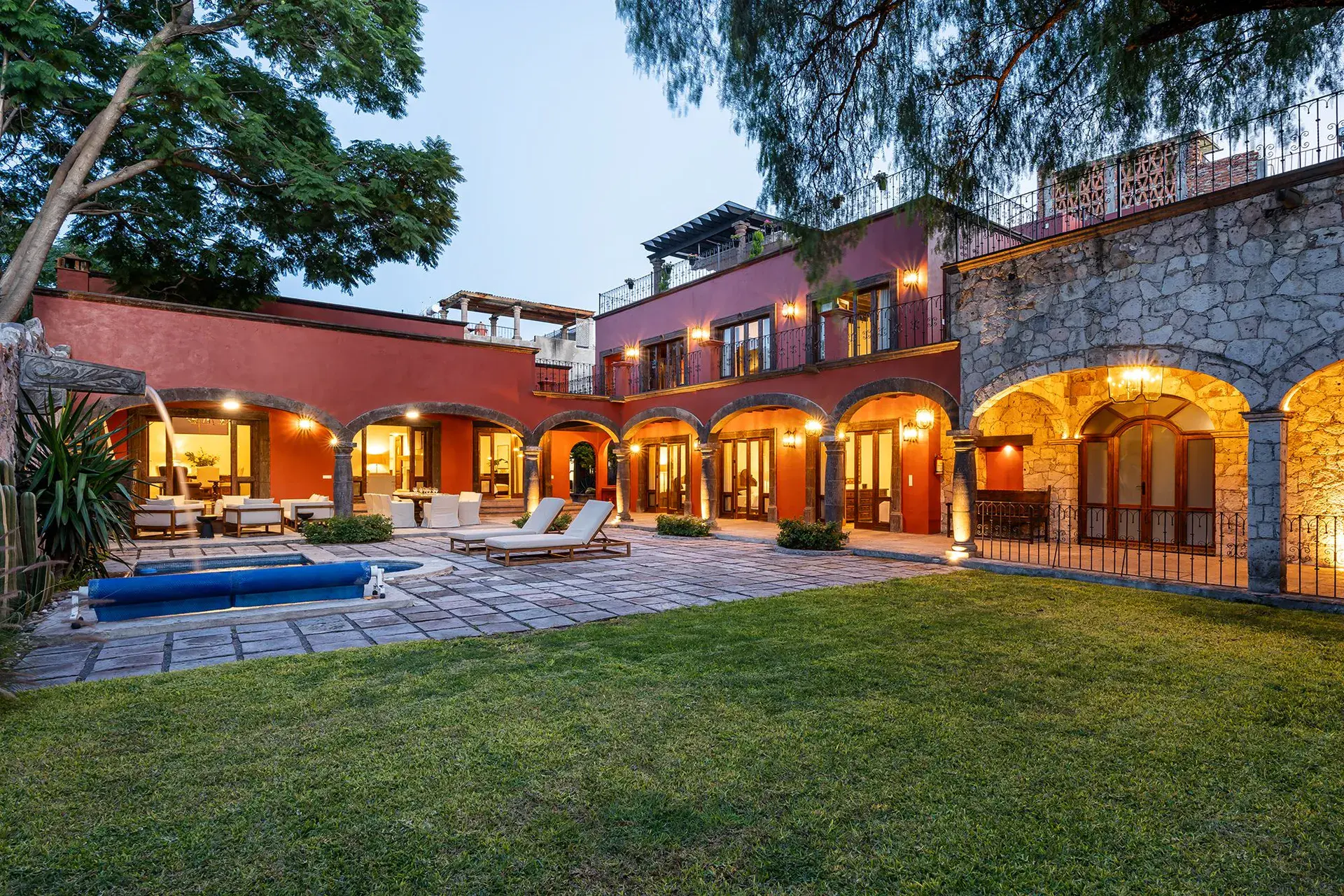 Casa Del Cardo, red facade with arched windows, a lawn and a pool at dusk, San Miguel de Allende