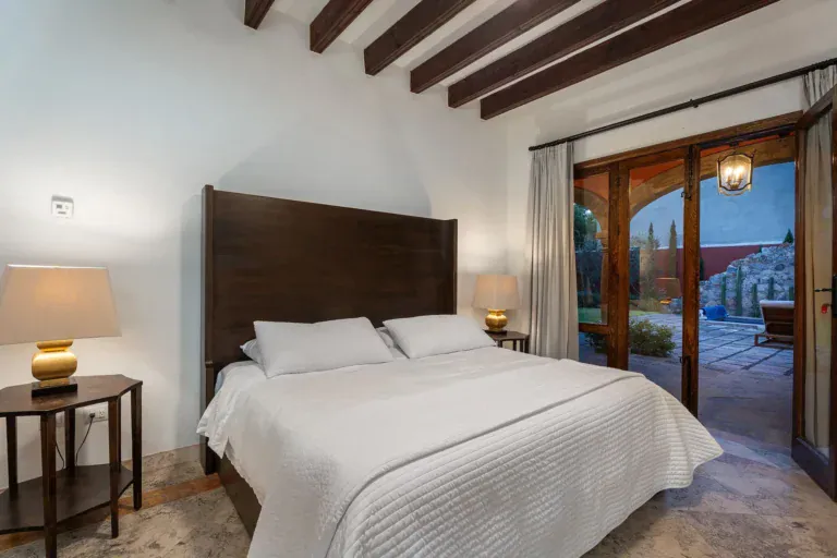 Casa Del Cardo, bedroom with a dark wood headboard and glass doors to the courtyard, San Miguel de Allende