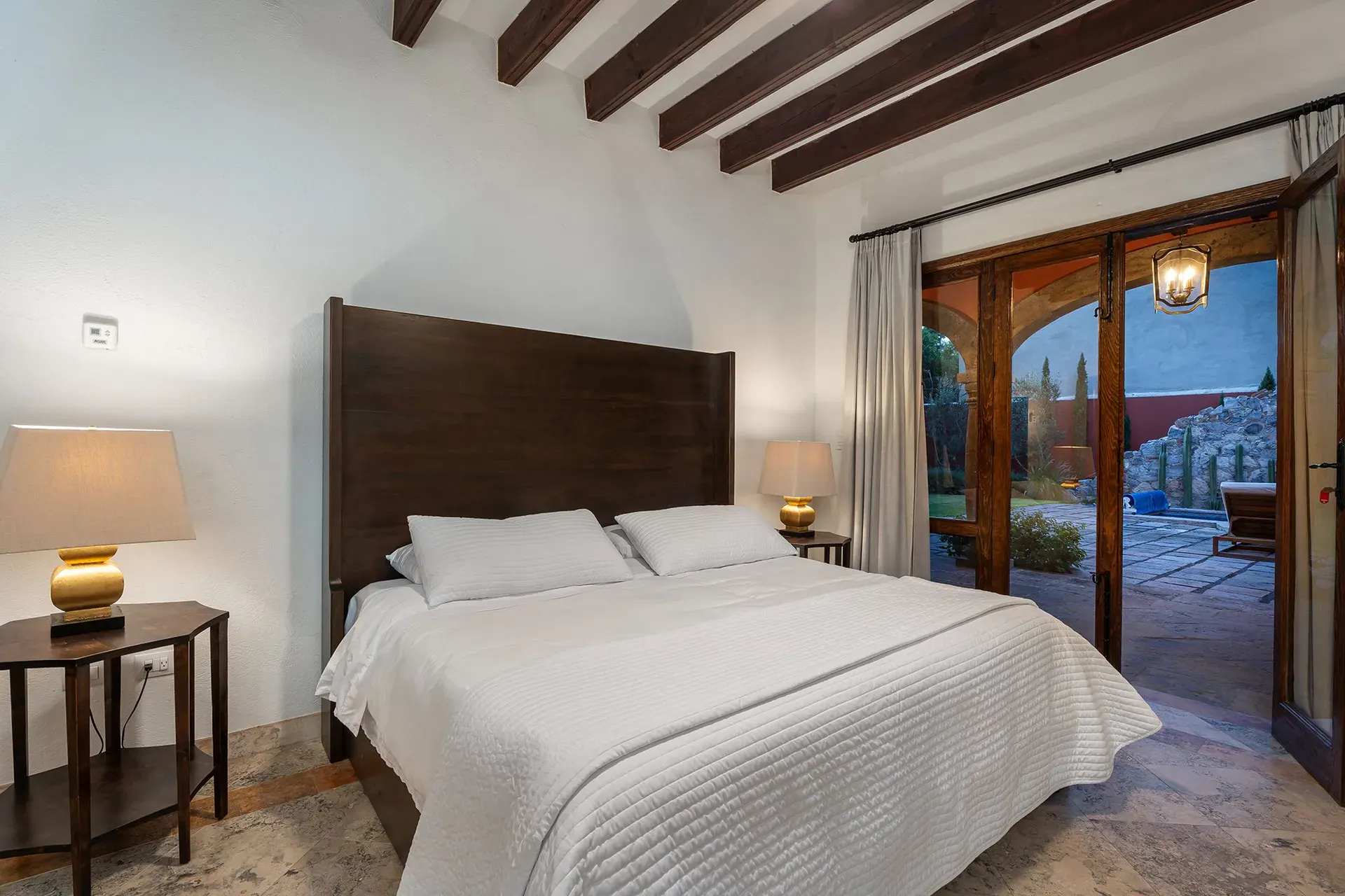 Casa Del Cardo, bedroom with a dark wood headboard and glass doors to the courtyard, San Miguel de Allende