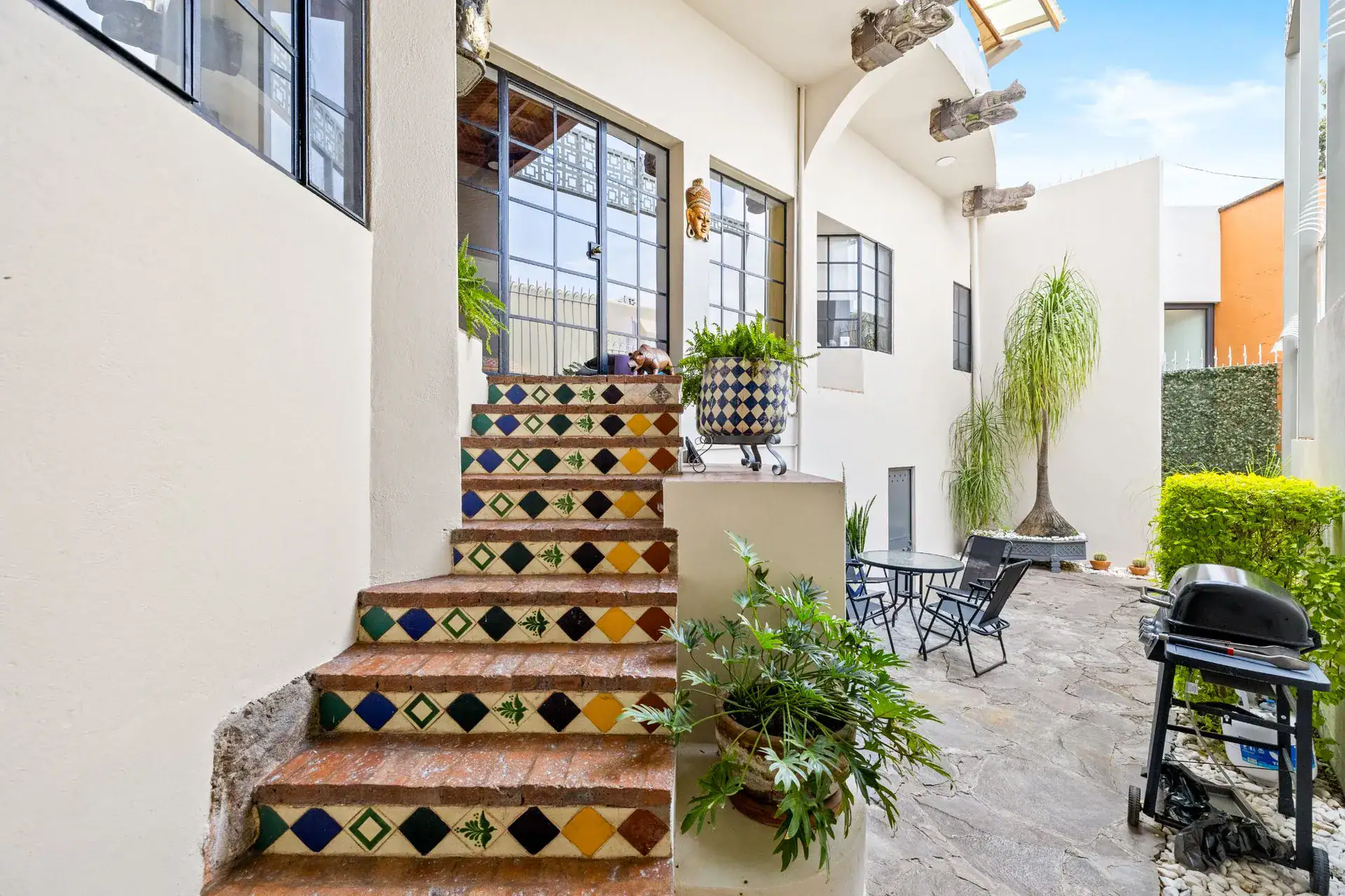 Casa del Foro, patio with a tiled staircase, a barbecue and bistro chairs beside white walls, San Miguel de Allende