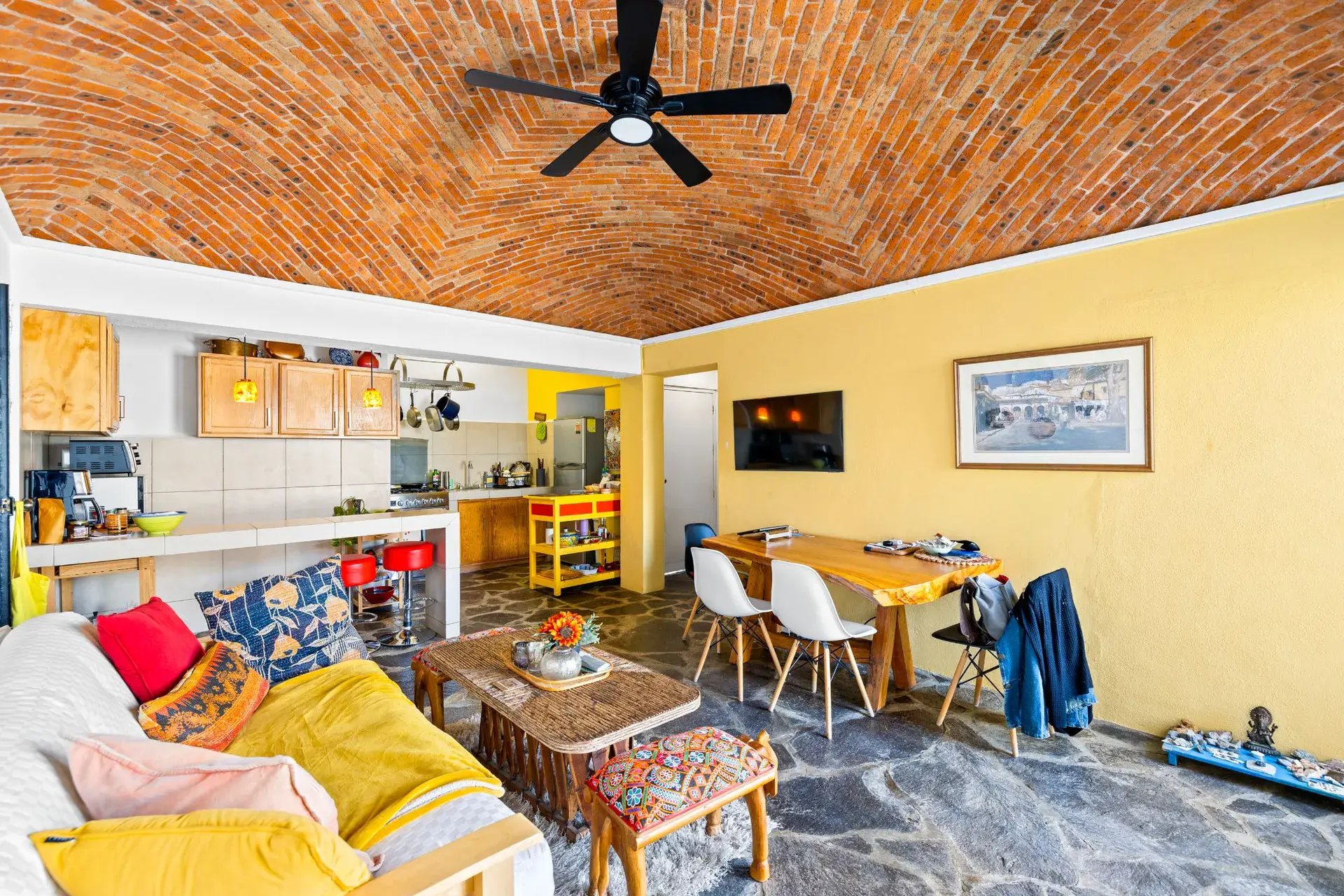 Casa del Foro, guest suite with a yellow kitchen, a sofa and a stone floor under a brick vaulted ceiling, San Miguel de Allende