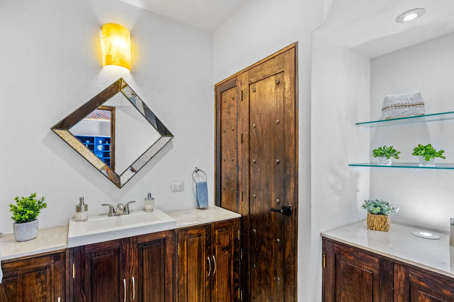 Casa del Foro, powder room with a diamond-shaped mirror, a carved wood door and glass shelves, San Miguel de Allende