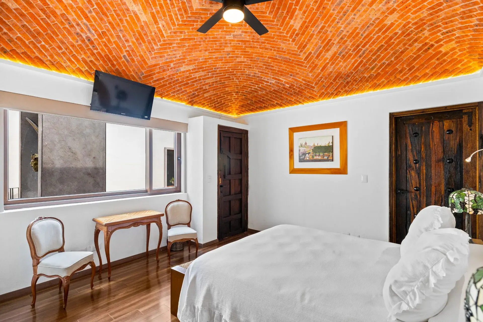 Casa del Foro, bedroom with a wall-mounted television, a window to the hallway and a carved wood door, San Miguel de Allende