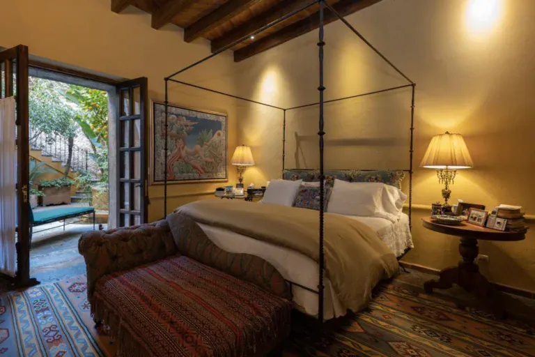 Casa Diana, bedroom with a black iron four-poster bed and a woven bench, San Miguel de Allende