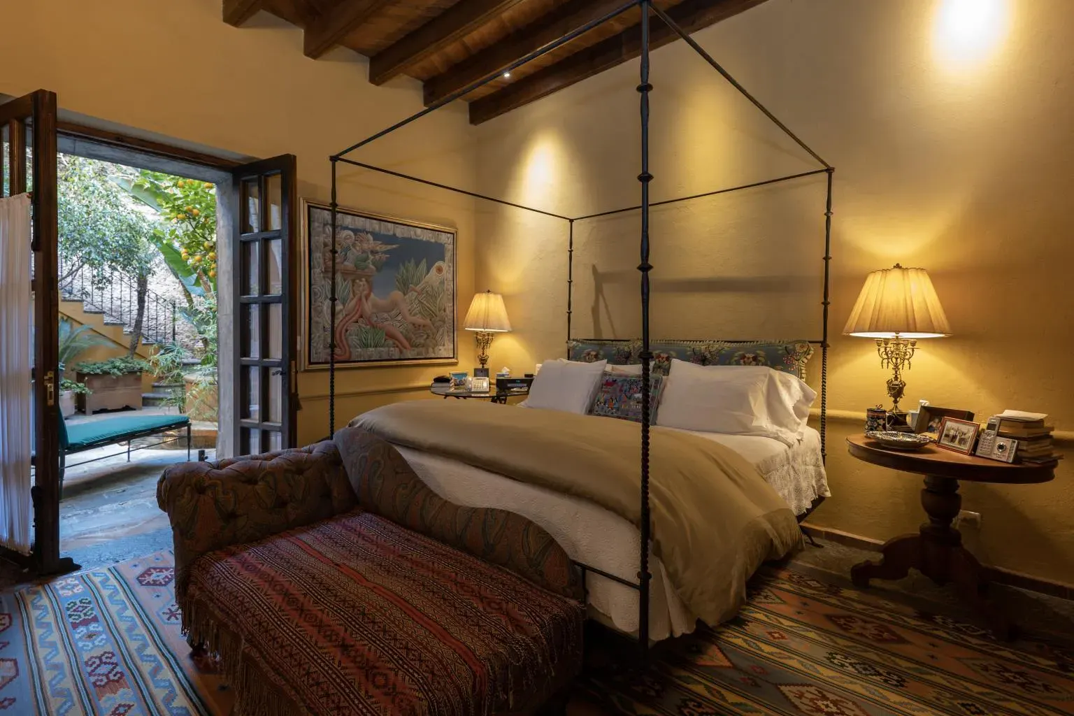 Casa Diana, bedroom with a black iron four-poster bed and a woven bench, San Miguel de Allende