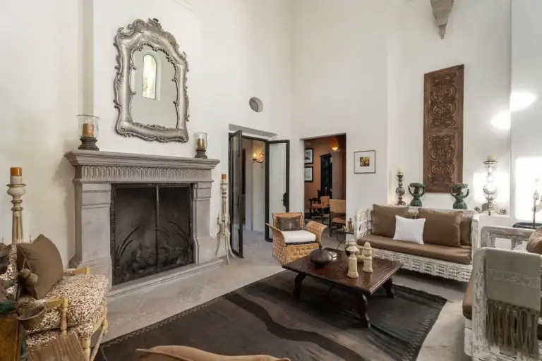 Casa Dos Casas, living room with a stone fireplace, ornate mirror, sofas and a dark rug under a high ceiling, San Miguel de Allende