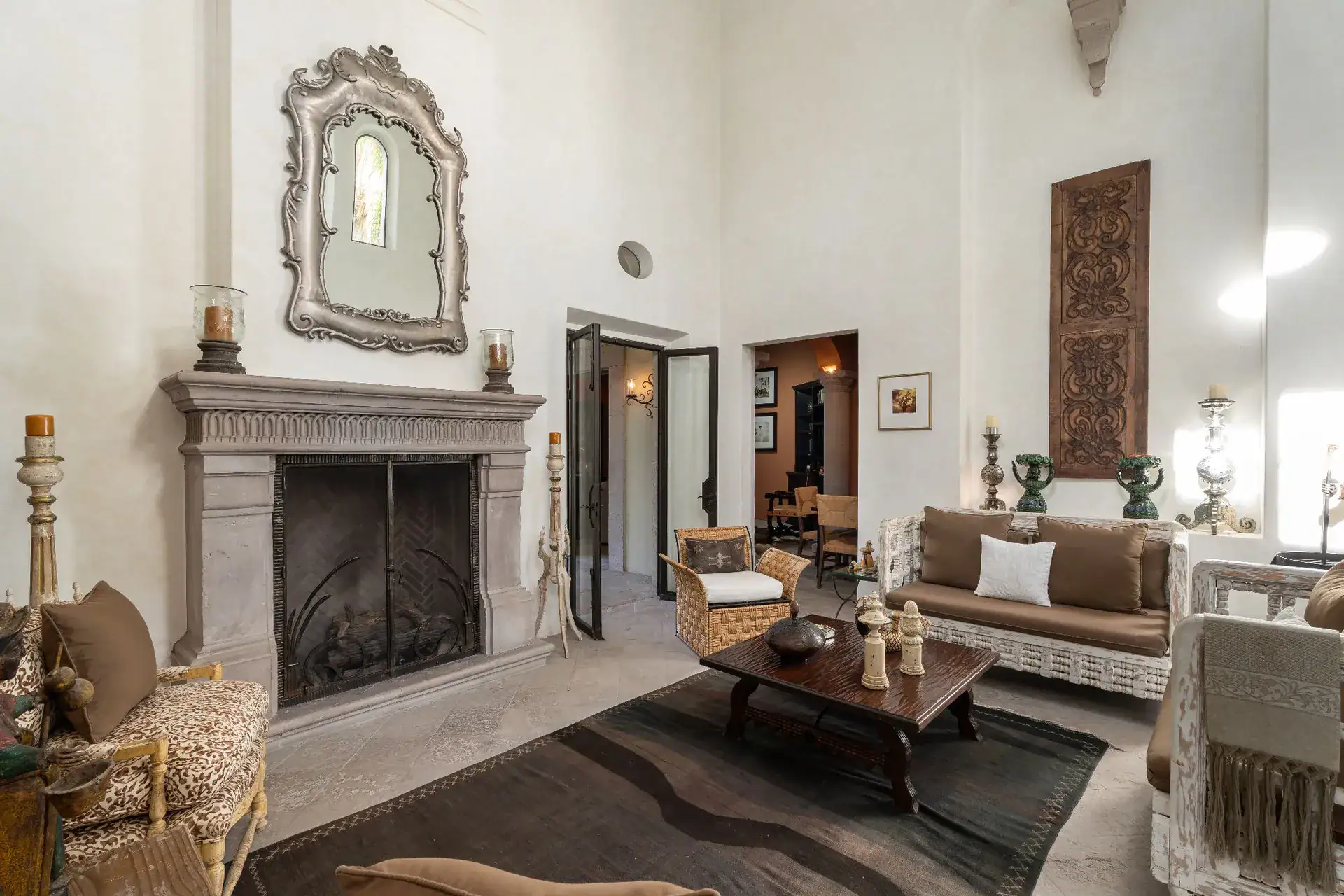 Casa Dos Casas, living room with a stone fireplace, ornate mirror, sofas and a dark rug under a high ceiling, San Miguel de Allende