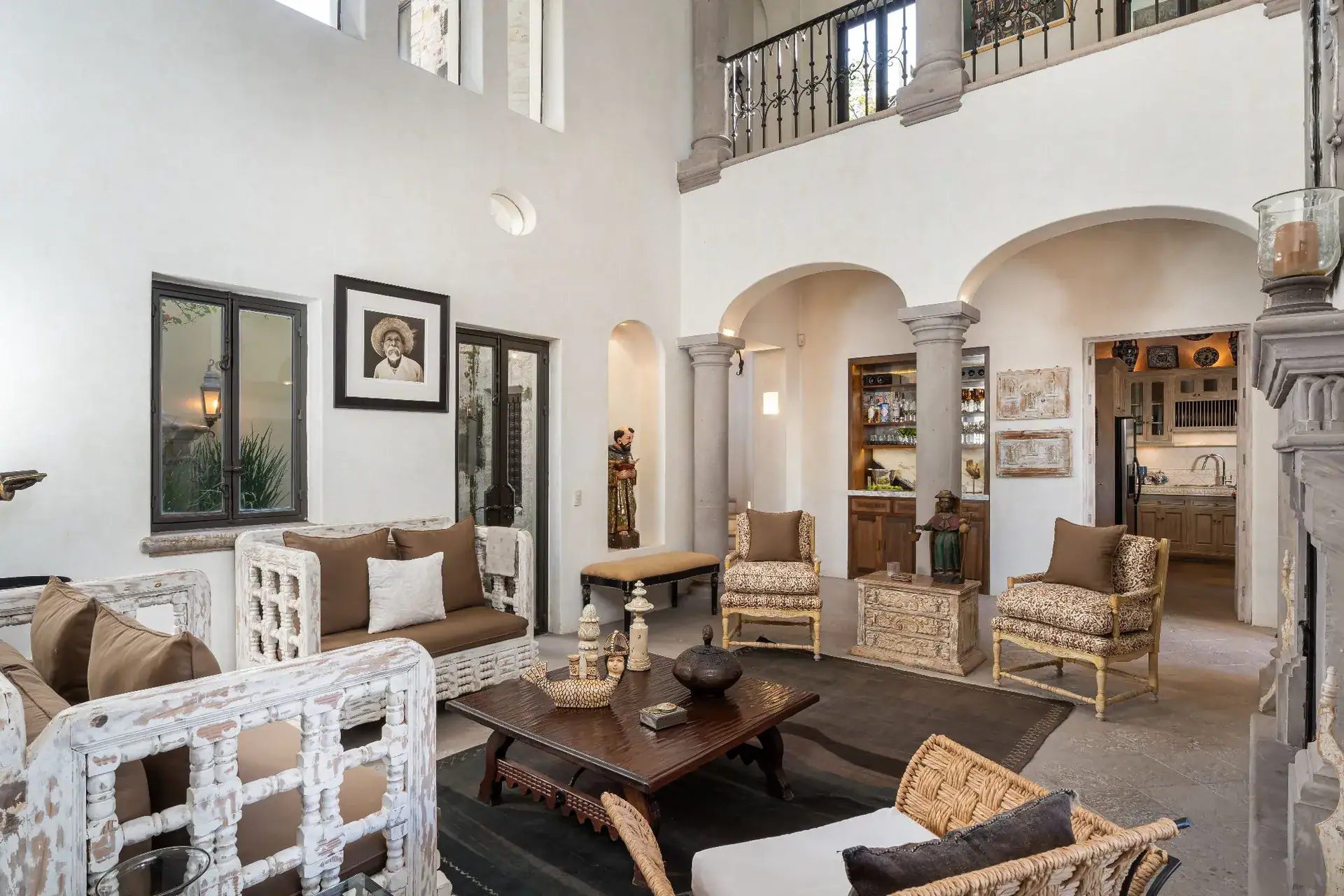 Casa Dos Casas, double-height living room with arches, a balcony above and wicker seating around a coffee table, San Miguel de Allende