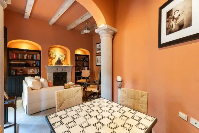 Casa Dos Casas, terracotta-walled sitting room with arched ceiling beams, bookshelves and a tiled table, San Miguel de Allende