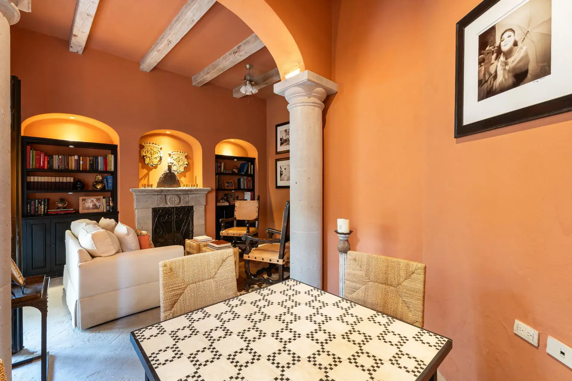 Casa Dos Casas, terracotta-walled sitting room with arched ceiling beams, bookshelves and a tiled table, San Miguel de Allende