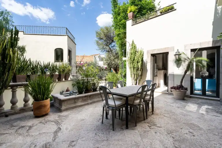Casa Dos Casas, sunny courtyard terrace with a tiled dining table, cacti and potted plants beside a white wall, San Miguel de Allende
