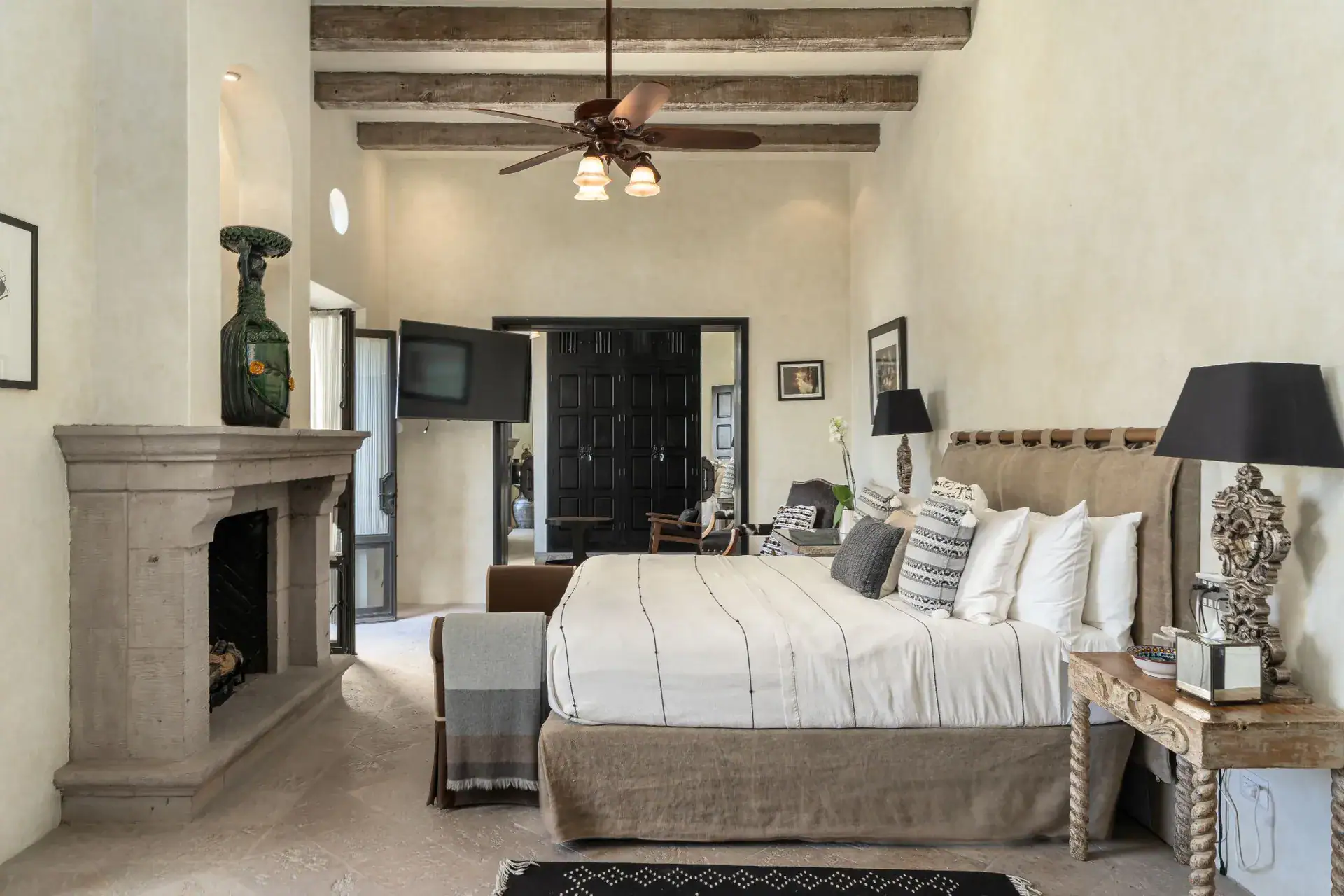Casa Dos Casas, bedroom with a king bed, stone fireplace and ceiling fan under a beamed ceiling, San Miguel de Allende