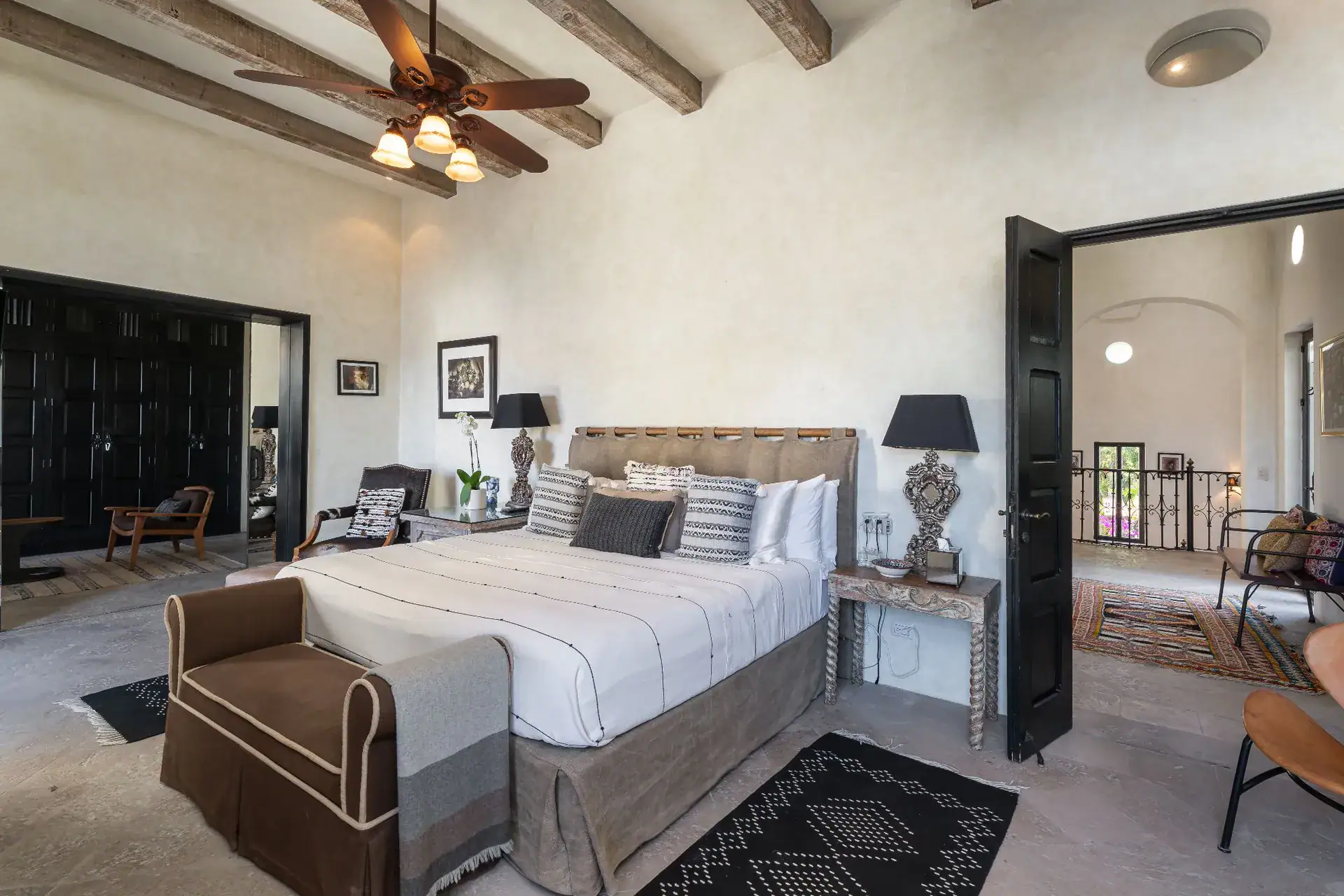 Casa Dos Casas, bedroom with a king bed, brown armchair and black-framed doors under a beamed ceiling, San Miguel de Allende